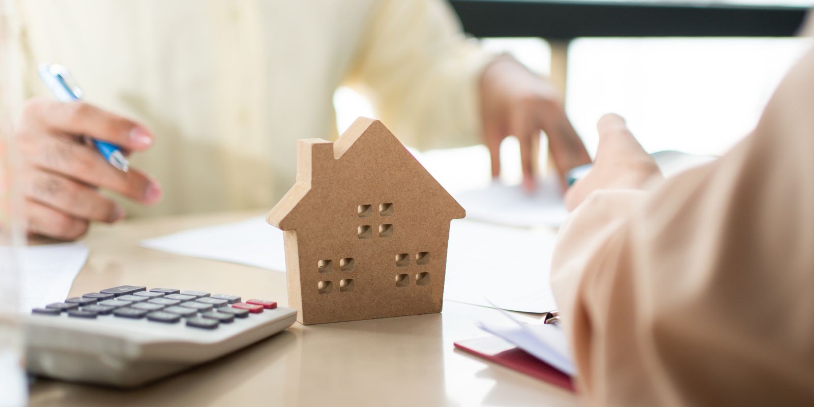 Person negotiating with another person across a desk with papers, calculator and a toy house