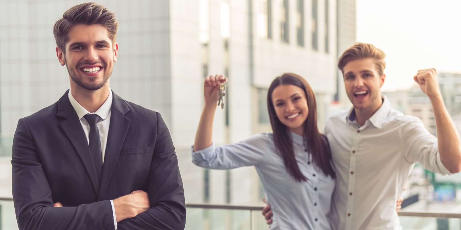 Happy couple holding a house key, beside a happy real estate agent.